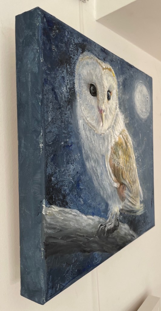 Sideview of an acrylic painting of an owl by Debbie Storey hanging on a white wall